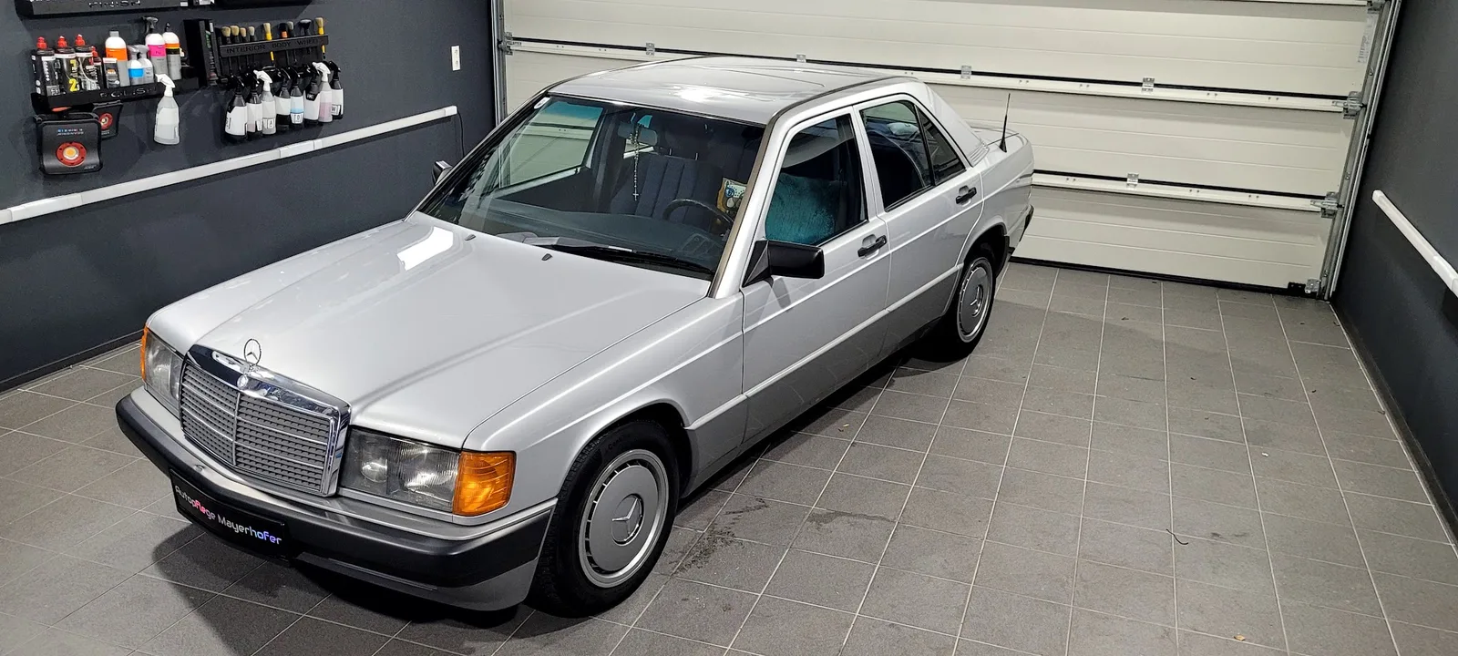 Frisch polierter silberner Mercedes 190 in der Werkstatt, an der Wand die Halterung mit den Politurmitteln