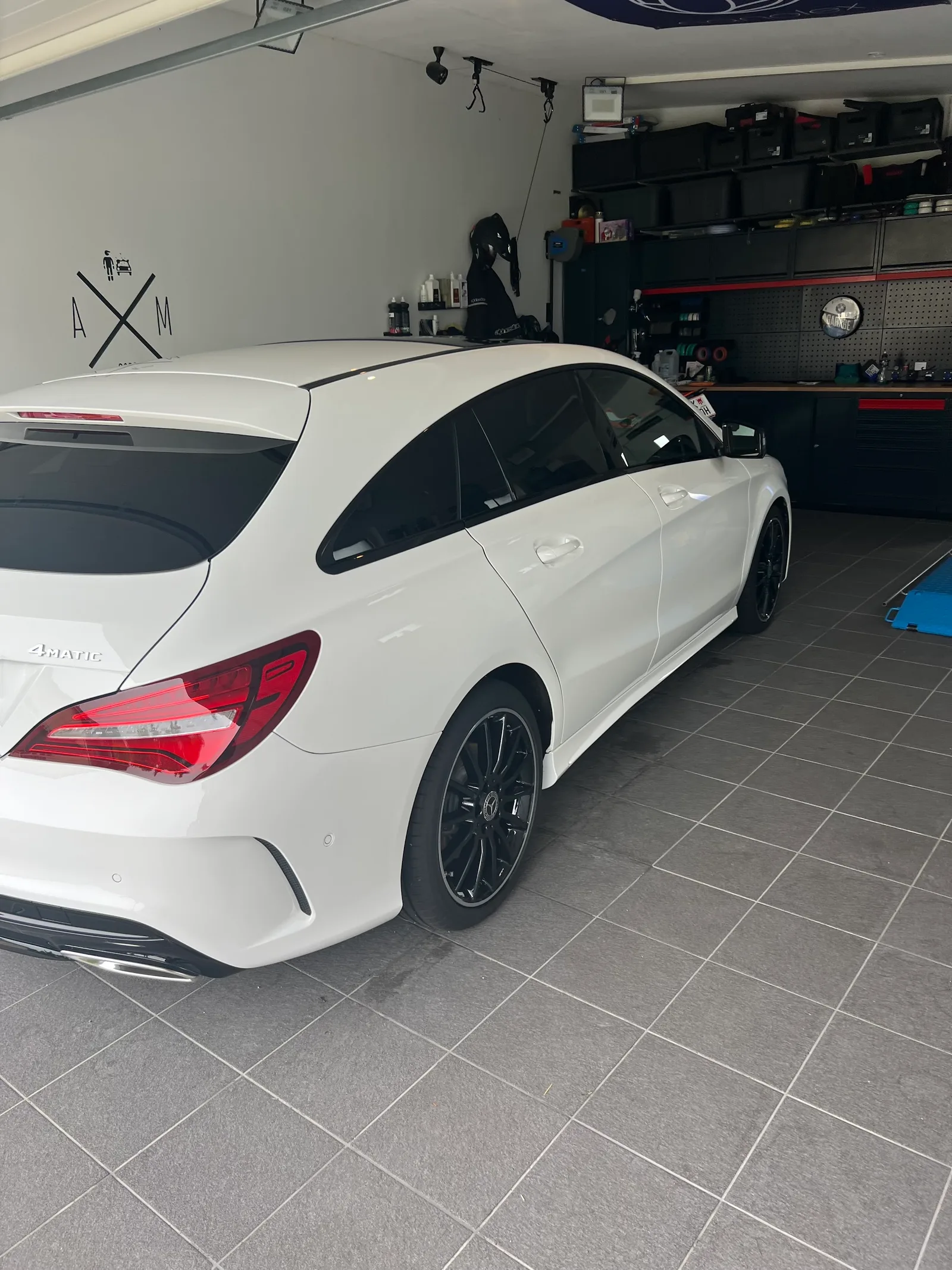 Weißer Mercedes CLA von hinten in der Werkstatt, an der Wand das Zeichen A mal M, im Hintergrund die Werkbank