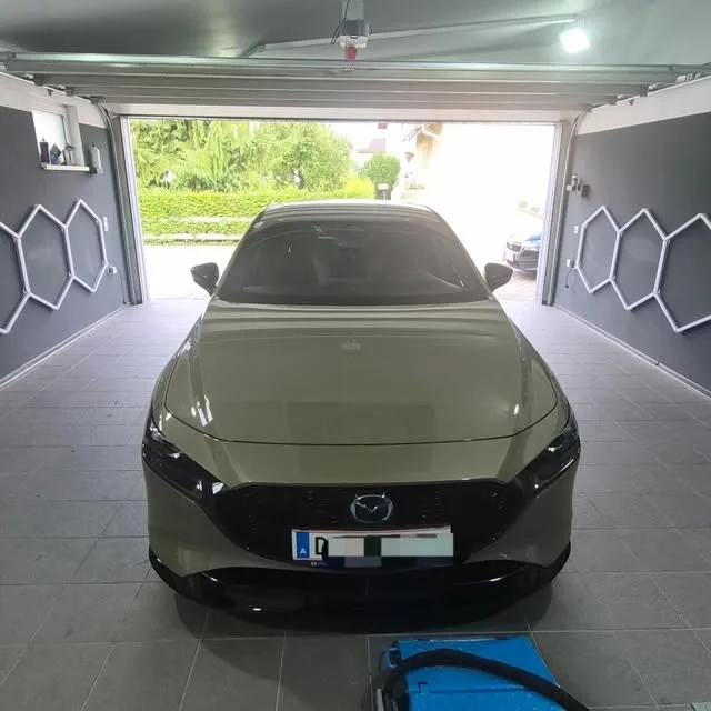 Grauer Mazda3 im offenen Tor der Werkstatt, beidseitig die beleuchteten Wabenelemente an der Wand