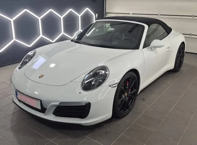 Weißer Porsche 911 Carrera Cabrio in der Werkstatt vor der beleuchteten Wabenwand